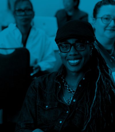 Jamie Allison smiles at the camera while sitting at a table in a breakout session at a conference.
