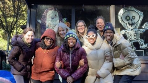A group of eight women smiling in a group photo outside