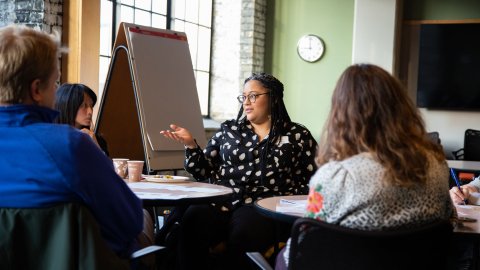 Woman pointing to flip chart at a table with colleagues