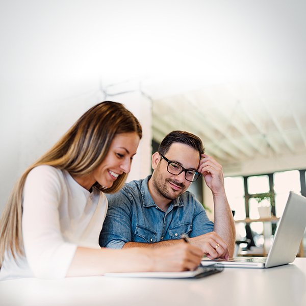 Man and woman sitting at desk smiling and looking at computer