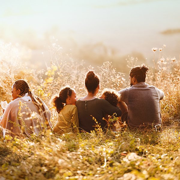 Multigenerational family sitting in field of wildflowers. Photo is taken of their backs.