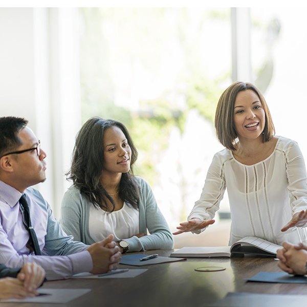 Colleagues in business attire at a conference room table with paper and pens in front of them. 