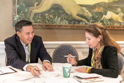 A man and a woman sitting at a table conversing and taking notes