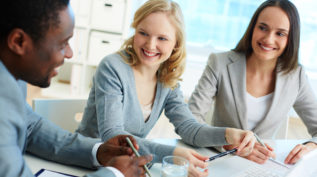 Two women and a man sit at a table, where two woman are clearly advising the man on a topic