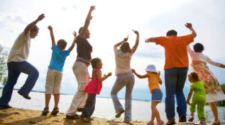 A family throws their hands up in joy on the beach; the photo is taken from the back and with an unfocused lens