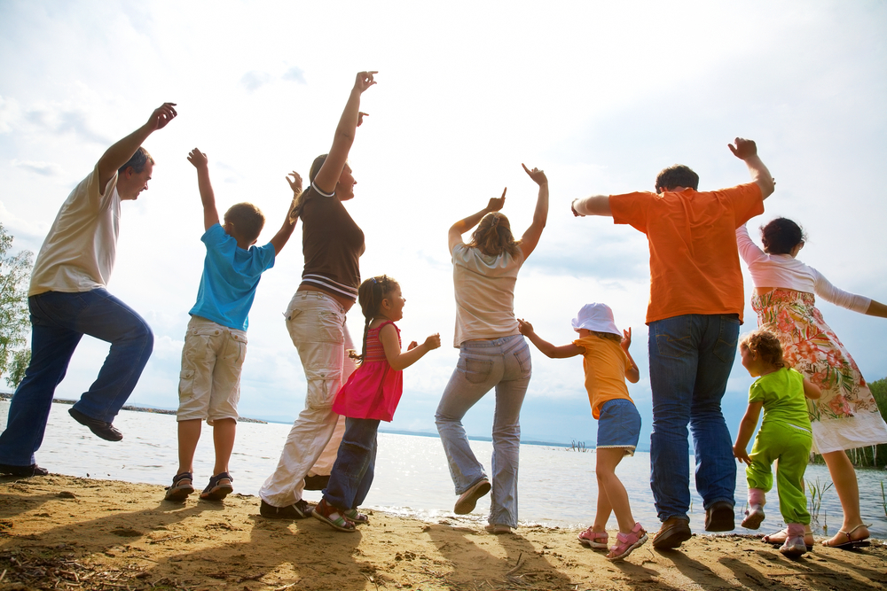 A family throws their hands up in joy on the beach; the photo is taken from the back and with an unfocused lens