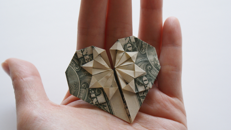 A hand holds a dollar bill that is shaped like an origami heart