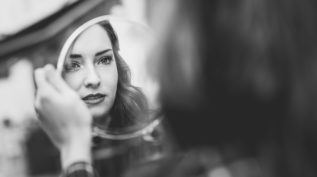 a white woman looks in a mirror; in grayscale