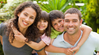 a family of two parents and two kids smiles at the camera