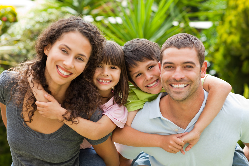 a family of two parents and two kids smiles at the camera