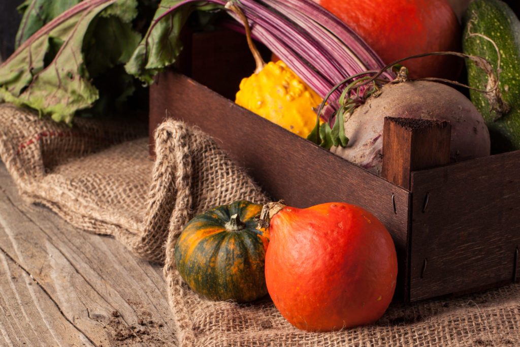 Colorful pumpkins and fresh beet in box on old wooden table with sackcloth