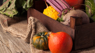 Colorful pumpkins and fresh beet in box on old wooden table with sackcloth