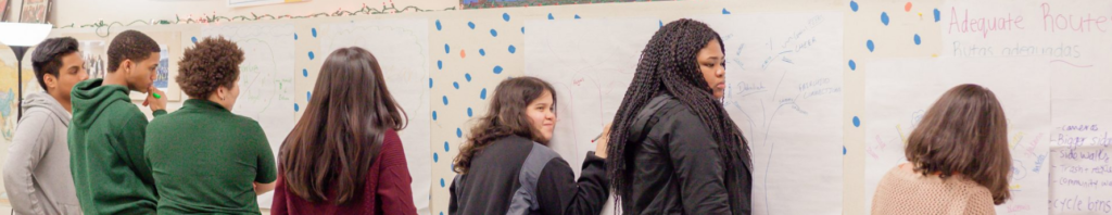 A group of young children write on a whiteboard