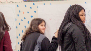 A group of young children write on a whiteboard