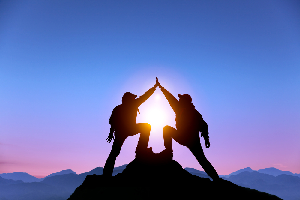 two climbers high five at the top of a mountain