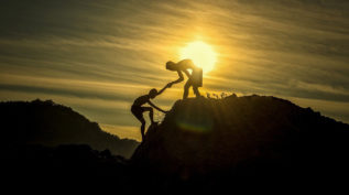 Person helping another person climb a mountain
