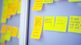Several bright yellow post its with indistinguishable writing a posted to a grey wall