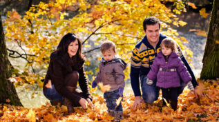 a family with kids plays in a pile of autumn leaves