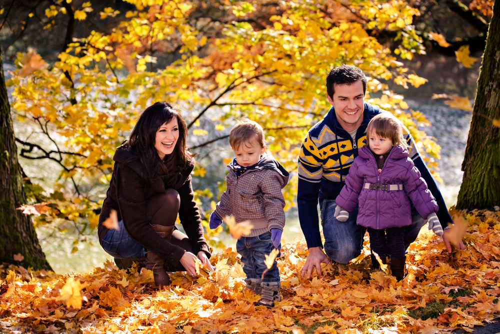 a family with kids plays in a pile of autumn leaves