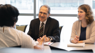 two people sit across a table from another person in a work environment