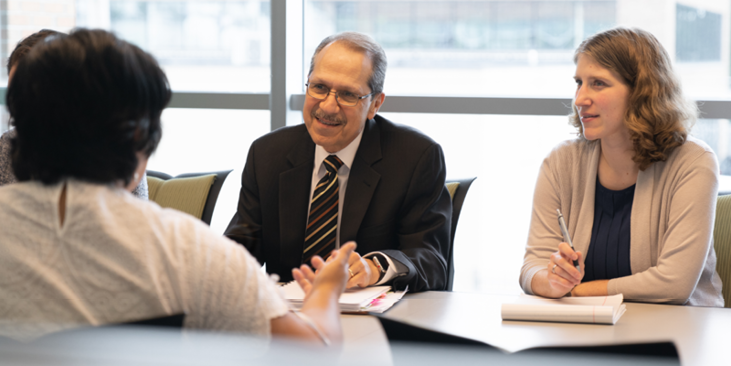 two people sit across a table from another person in a work environment