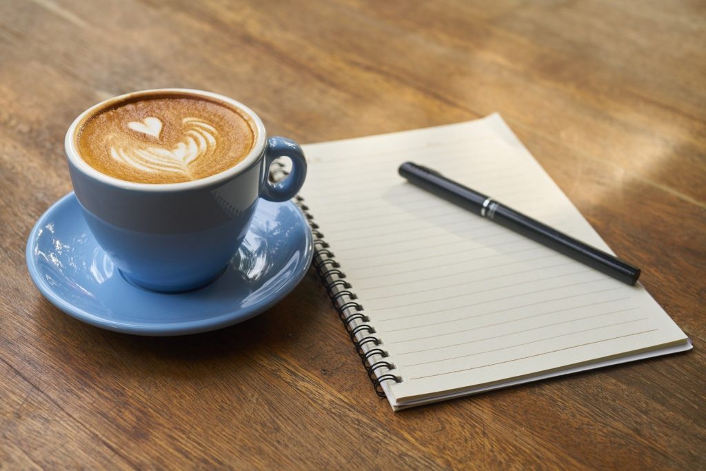 a cup of coffee sits next to a notebook and pen on a wooden table