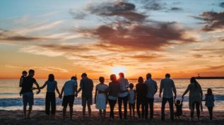 A large group of people standing on the beach, silhouetted by the sunset