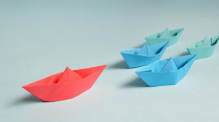 four paper boats with a red boat leading the way