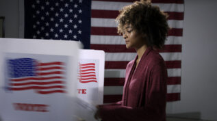 Black woman at voting polls with American flag in the background