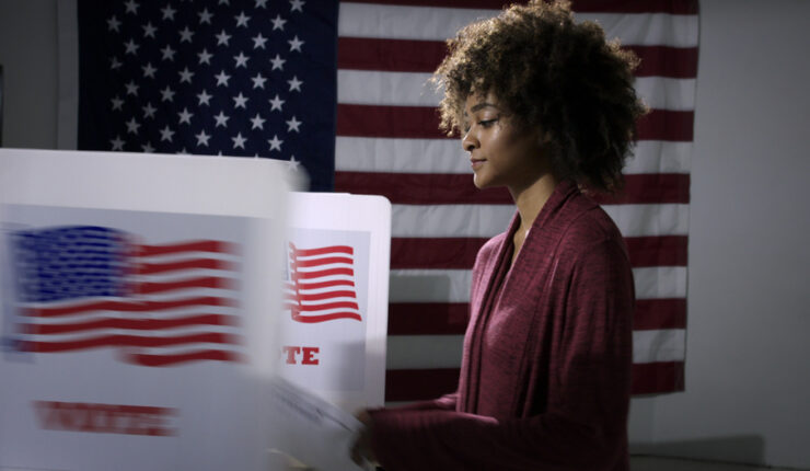 Black woman at voting polls with American flag in the background