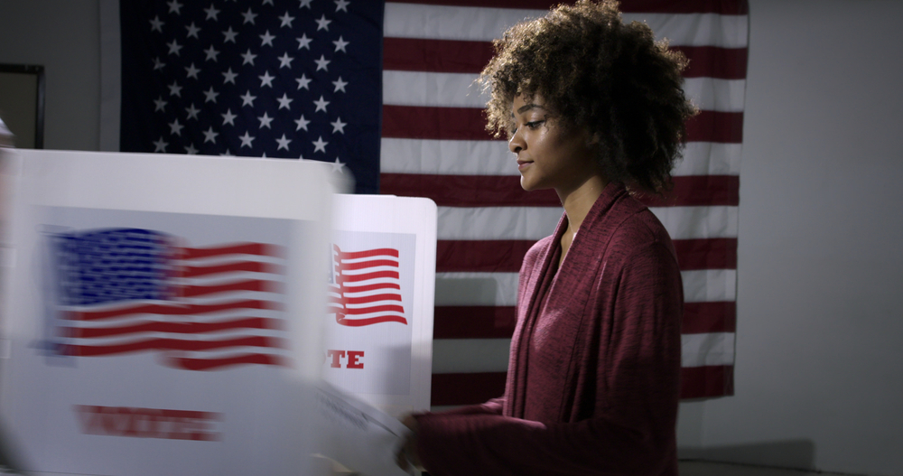 Black woman at voting polls with American flag in the background