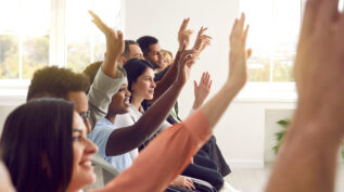 diverse group of people seated and raising their hands