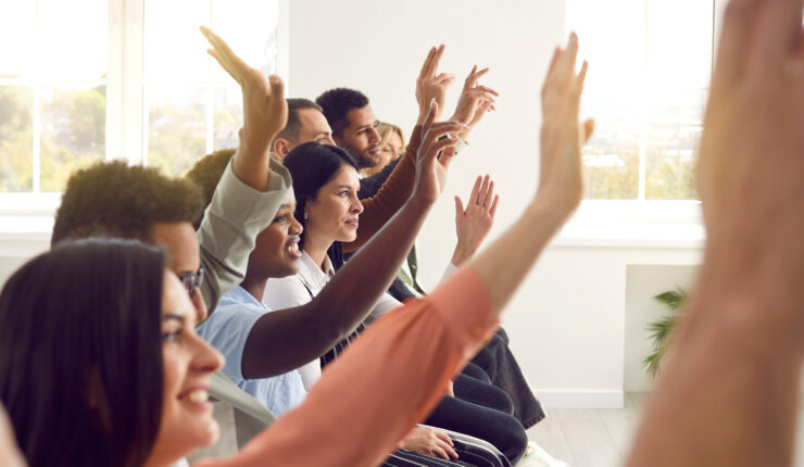 diverse group of people seated and raising their hands