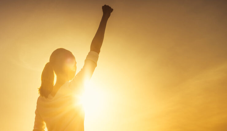 silohuette of woman in sunset raising fist in air