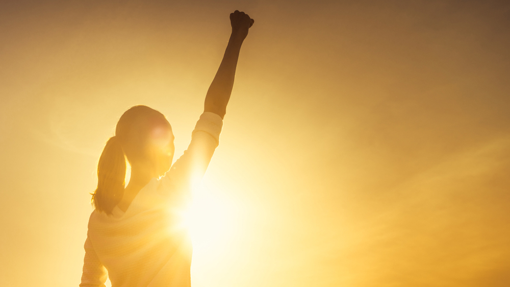 silohuette of woman in sunset raising fist in air