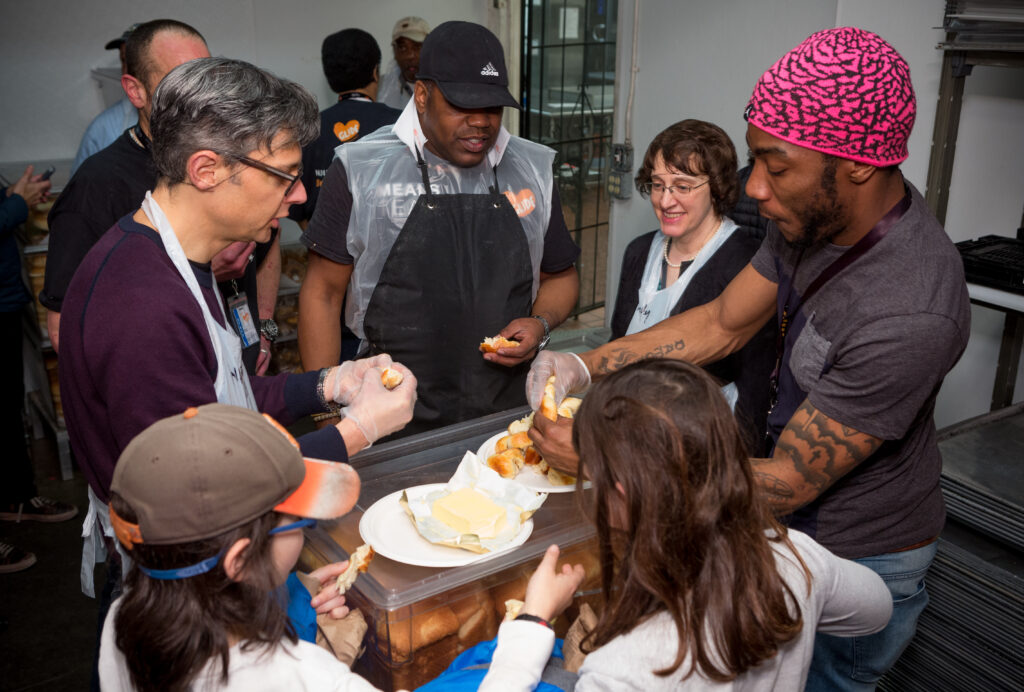 a multigenerational, multi-ethnic group of kitchen volunteers gather around to share freshly baked challah bread